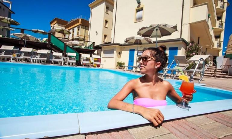 Femme dans la piscine avec cocktail, journée ensoleillée.
