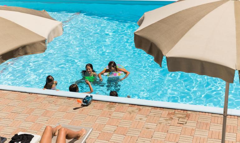 Piscine avec enfants jouant et parasols beiges.